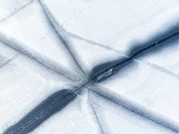 Légi drón tetején kilátás hó borított fagyasztott tó vagy folyó felszínén nagy repedt jég átlós vonalak. Természetes téli táj elvont textúra minta. Veszélyes tó olvadás az olvadási időszakban — Stock Fotó