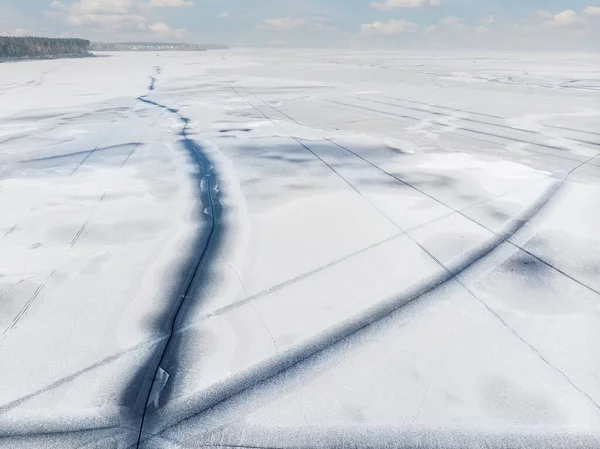 Vista superior do drone aéreo da neve coberta lago congelado ou superfície do rio com grandes linhas diagonais de gelo rachado. Paisagem de inverno natural padrão de textura abstrata. Lagoa perigosa derretendo na estação de degelo — Fotografia de Stock