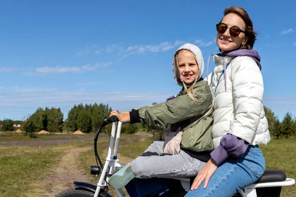 Fiatal felnőtt gyönyörű anya és lánya élvezik a szórakozást lovaglás elektromos robogó kerékpár vagy vidéki vidéki földút fényes napos napon. Anya a gyermek közúti utazás természet kaland utazás dobropark — Stock Fotó