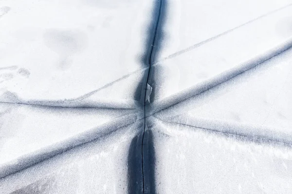 Aerial drone top view of snow covered frozen lake or river surface with big cracked ice diagonal lines. Natural winter landscape abstract texture pattern. Dangerous pond melting at thaw season — Stock Photo, Image