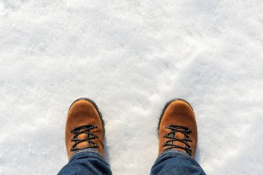 Üst tarafta kot pantolon giymiş erkek bacakları ve beyaz buzlu kar yüzeyinde izole edilmiş kahverengi deri çizmeler var. Su geçirmez ayakkabılar. Kış yürüyüşü ve doğa yürüyüşü kavramı