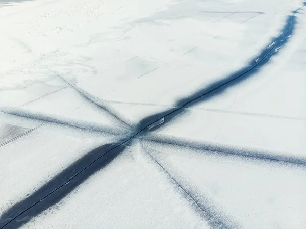 Letecký bezpilotní letoun shora pohled na sníh pokrytý zamrzlé jezero nebo říční hladinu s velkými popraskané led diagonální čáry. Přírodní zimní krajina abstraktní textury vzor. Nebezpečné tání jezírka v období tání — Stock fotografie