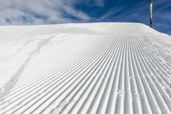 Close-up straight line rows of freshly prepared groomed ski slope piste with bright shining sun and clear blue sky background. Snowcapped mountain downhill landscape at europe winter skiing resort — Stock Photo, Image