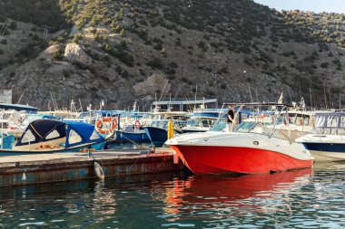 Pek çok balıkçı teknesi ve kiralık sürat teknelerinin dağ limanı göl körfezine demir attığı manzara güneşli gündoğumu sabahında, güneşli güneşin arkadan vurduğu sıcak güneşe karşı. Deniz marinası teknesi, alacakaranlık vakti.