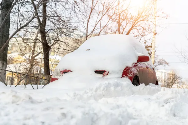 City street driveway parking lot spot with small car covered snow stuck trapped after heavy blizzard snowfall winter day by big snowy pile. Snowdrifts and freezed vehicles. Extreme weather conditions — Stock Photo, Image
