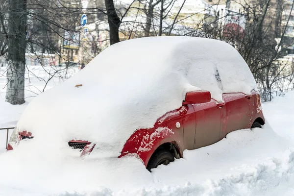 City street driveway parking lot spot with small car covered snow stuck trapped after heavy blizzard snowfall winter day by big snowy pile. Snowdrifts and freezed vehicles. Extreme weather conditions — Stock Photo, Image