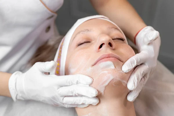 Közelkép kozmetikus orvos kezét, hogy anti-age eljárás, maszk és peeling fiatal vonzó női ügyfél a kozmetikai klinikán. Kozmetológus szakorvos bőrápoló kezelést végez. Egészségügyi kezelés — Stock Fotó