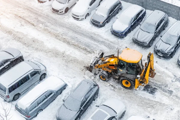 A traktorrakodó gép piszkos havat tölt fel a szemétszállító kocsira. A város utcájának megtisztítása, a hó és a jég eltávolítása nehéz hóesések és hóvihar után. Hóeke szabadban tiszta járda járda út felhajtó — Stock Fotó