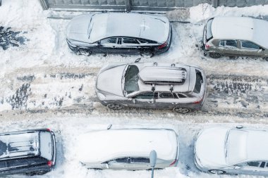 Çatı rafı bagajı olan, şehir caddesinde park etmiş araçların arasından geçen, buzlu kış gününde yoğun karla kaplı, modern arazi aracının hava manzarasının üstünde. Apartman yolu.