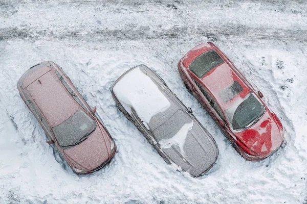 Vista aérea superior del estacionamiento del edificio de oficinas de apartamentos con muchos coches cubiertos de nieve escondida después de la fuerte nevada nevada el día de invierno. Deriva de nieve y vehículos congelados. Condiciones meteorológicas extremas —  Fotos de Stock