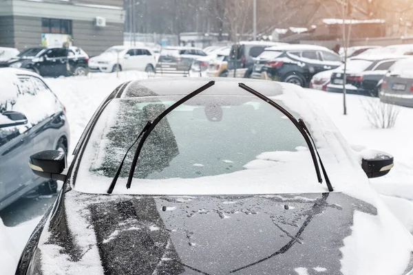 Közelkép részlet kilátás fekete modern autó emelt fel szélvédő ablaktörlő pengék, hogy megakadályozzák a jegesedés hideg fagyos téli napon. Jármű szélvédő fedett whote hó parkol a város utcájában a szabadban — Stock Fotó
