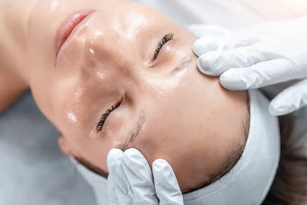 Close-up beautician doctor hand making anti-age procedure massage peeling for young attractive female client at beauty clinic. Cosmetologist specialist doing skincare treatment. Health care therapy — Foto Stock