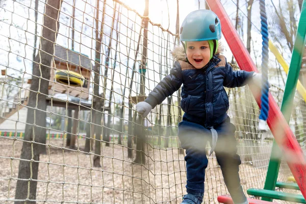 Portrait happy brave courage little toddler child boy wear safety equipment helmet enjoy passing obstacle course forest rope adventure park on cold winter day. Active outside leisure amusement camp