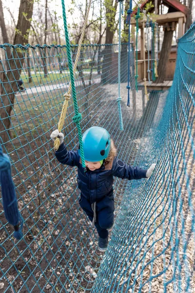 Retrato feliz coraje valiente niño pequeño niño niño usar equipo de seguridad casco disfrutar de pasar carrera de obstáculos bosque cuerda aventura parque en frío día de invierno. Activo fuera de campamento de entretenimiento de ocio —  Fotos de Stock