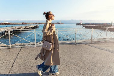 Genç, modaya uygun, şık, güzel, beyaz, mutlu bir kadın sıcak, güneşli bir günde Yalta deniz kenarında yürümeyi seviyor. Kadın portresi şehir caddesinde kot pantolon giyer.