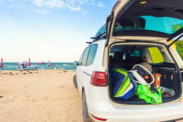 Tillbaka visa unga vuxna manliga surfare i våtdräkt sätta ut surfbräda kite utrustning på sandstrand från van fordon med takbox hav strand vattensport plats läger.Äventyr resor sport aktivitet — Stockfoto