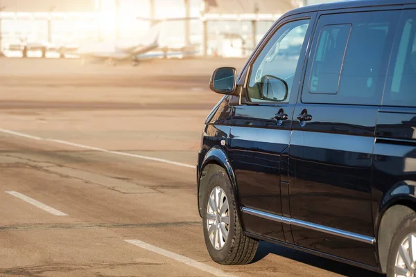 Havaalanı taksisinde çalışan siyah VIP servis minibüsünün yan görüntüsü ve arka planda terminal binası var. Havaalanında birinci sınıf taksi servisi. Güvenlik İstihbarat Teşkilatı havaalanında acele ediyor.