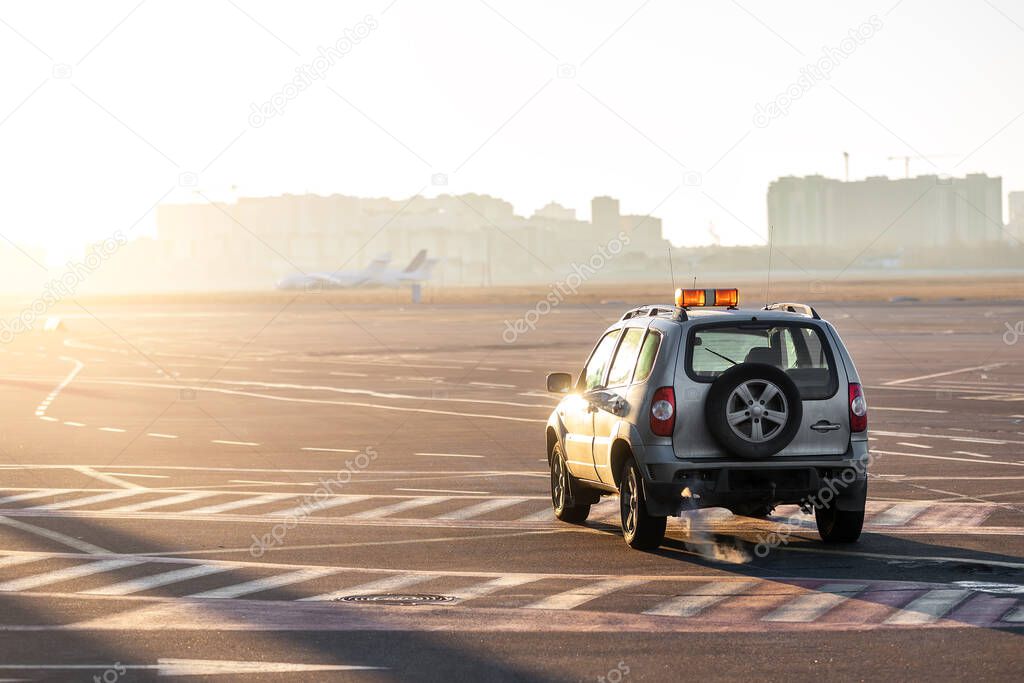 Scenic view of airport security car on tarmac apron taxiway in warm sunlight of bright morning sunrise or evening sunset time. Follow me safety vehicle staff. Aviation maintenance and service machine