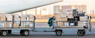 Turboprop kargo uçağına karşı ticari paketlerle dolu kargo vagonunun yakın çekim görüntüsü. Hava postası ve lojistik. Dışarıya aktarma işlemleri. Ticari charter uçuş servisi