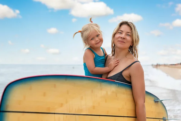 Νέοι ενήλικες λεπτό σπορ θηλυκό surfer κορίτσι απολαμβάνουν τη διασκέδαση κολύμπι μαζί με χαριτωμένο κοριτσάκι surfboard θάλασσα κύμα κύμα θάλασσα ηλιόλουστη μέρα. Αθλητισμός υγιή ξέγνοιαστες διακοπές τρόπο ζωής έννοια — Φωτογραφία Αρχείου