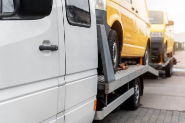 Beyaz, küçük, kargo kamyonu taşıyıcısı iki sarı minibüsle dolu, düz vagon platformunda ve yol kenarındaki otoyolda römork çekici. Ukraynalılar için gönüllü destek nakliyesi