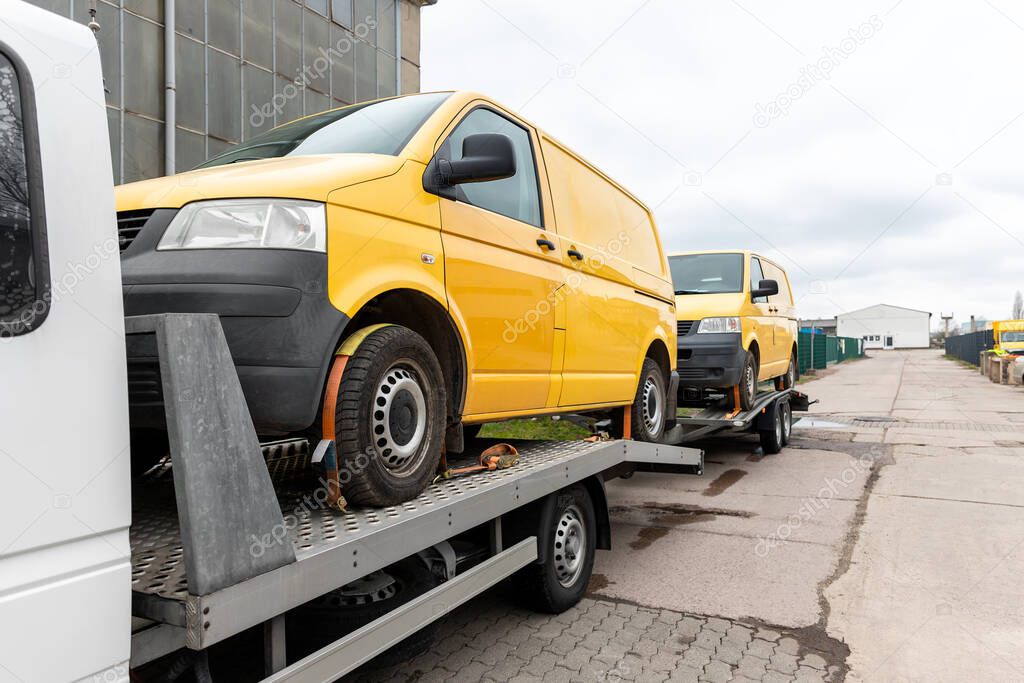 White small cargo truck car carrier loaded with two yellow van minibus on flatbed platform and semi trailer tow on roadside highway road. Volunteer support delivery transport for ukrainina people