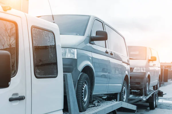 White small cargo truck car carrier loaded with two yellow van minibus on flatbed platform and semi trailer tow on roadside highway road. Volunteer support delivery transport for ukrainina people — ストック写真