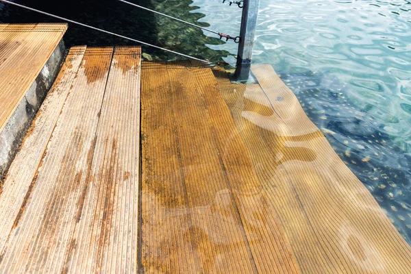 Vista de detalle de cerca de escalones de escalera de madera natural de escalera de alerce en agua azul limpia de lago, mar o estanque. Material de madera Waterpoof. Superficie de terraza de tablero a rayas a prueba de humedad — Foto de Stock