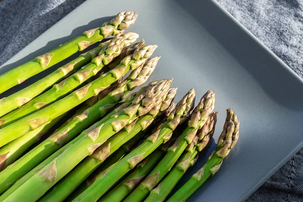 Primer plano detalle manojo de planta fresca de espárragos verdes crudos cosechados en temporada sobre fondo de cocina placa de cerámica azul. Vegetariano saludable comida vegetal gourmet. Salud dieta vegana concepto de nutrición — Foto de Stock