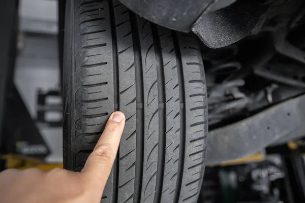 Mechanic pointing with hand at tyre wear indicator at car service center. Vehicle wheel protector control and inspection during maintenance. Tread wear check test inspection at automotive maintenance — Fotografia de Stock