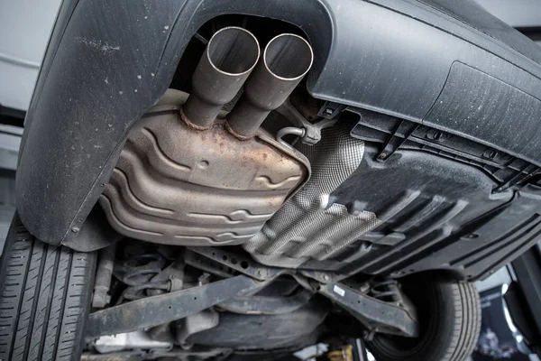 Close-up detail bottom view of car part metal exhaust muffler pipe with rusty stains. Lifted vehicle check-up maintenace service, repair and fix at automotive workshop — Foto de Stock