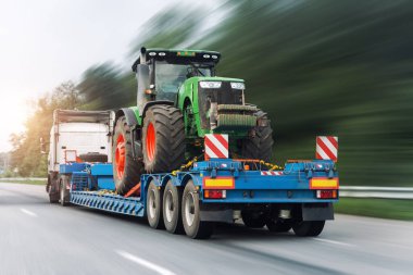 POV ağır sanayi kamyonunun yarı tırı platforma yanaştı. Büyük, modern bir tarım traktörü taşıdı. Parlak gökyüzünde ortak bir otoyol üzerindeydi. Tarım ekipmanları taşıma hizmeti.