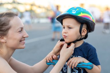 Yakın plan anne babası, yaz günü bisiklet sürdüğü ya da Scooter City Sokak Parkı 'nda gezdiği için sevimli sarışın, beyaz çocuk için kaskını takmış ve kaskını takmış. Çocuk sporları koruma hizmetleri.