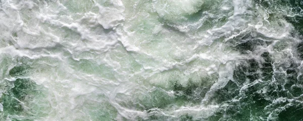 Close-up abstract texture above view of river torrent and clear fresh cold water flowing through mountain rocks in valley with foam and bubbles on sunny day. Nature force and power background.