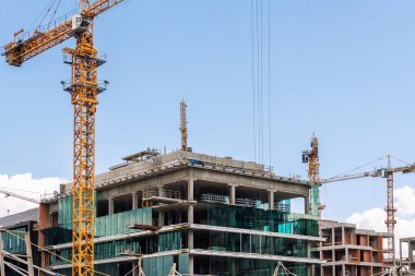 Gökyüzü arka planına karşı birçok yüksek kule vinci ve ağır makineleri olan modern apartman binası cam cephe inşaat alanı. Endüstriyel manzaralı şehir gelişim projesi.
