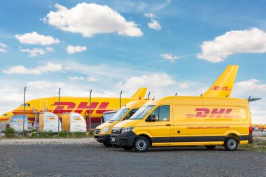 Schkeuditz, Almanya - 29 Mayıs 2022 - Leipzig Halle havaalanı terminalinde dağıtım için park etmiş kargo uçaklarına karşı birçok kurye minibüsü. DHL hava postası hızlı lojistik merkez terminali.