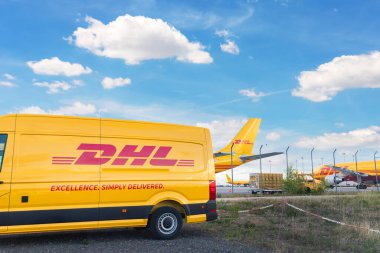 Schkeuditz, Almanya - 29 Mayıs 2022 - Leipzig Halle havaalanı terminalinde dağıtım için park etmiş kargo uçaklarına karşı birçok kurye minibüsü. DHL hava postası hızlı lojistik merkez terminali.