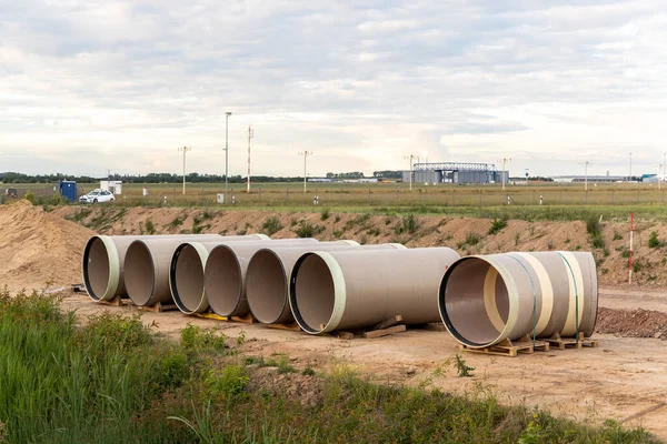 Stack of big frp composite fiberglass plastic sewage pipes at warehouse construction site near Leipzig Halle airport against blue sky background. Highway road construction infrastructure earthworks.