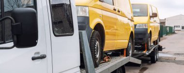 Beyaz, küçük, kargo kamyonu taşıyıcısı iki sarı minibüsle dolu, düz vagon platformunda ve yol kenarındaki otoyolda römork çekici. Ukraynalılar için gönüllü destek nakliyesi.