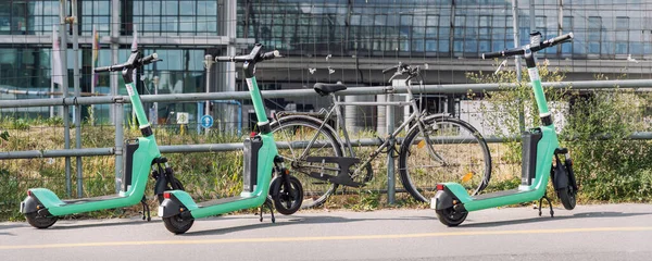 Many modern green electric scooters sharing parked city street. Self-service street transport rental service. Rent urban mobility vehicle with smartphone application. Zero emission green eco energy.