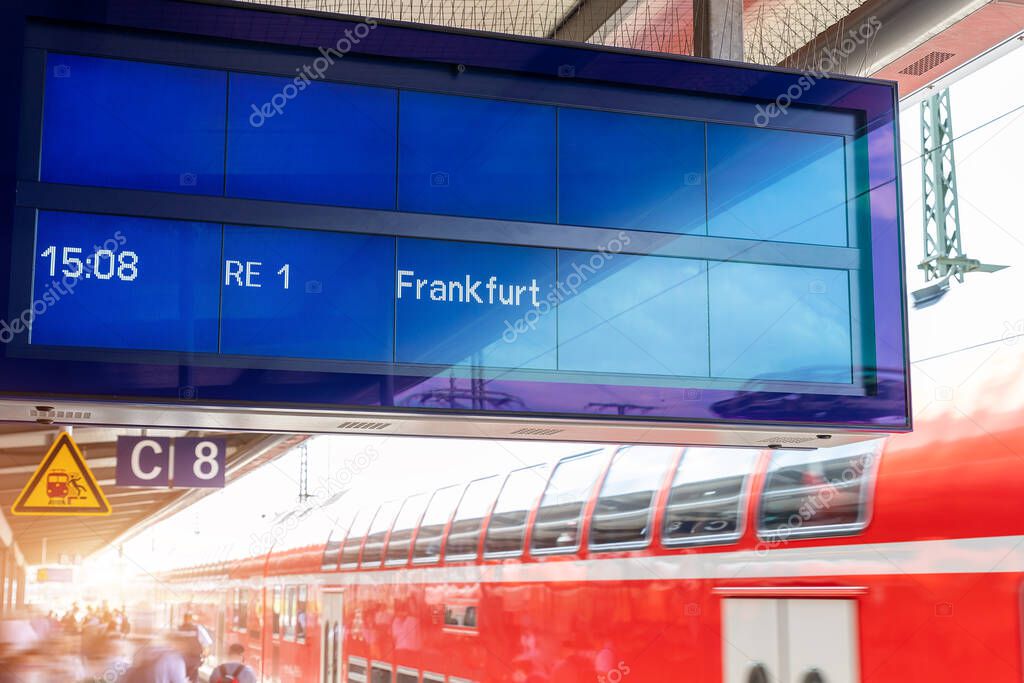 Close-up sign data information timetable digital display board against fast moving modern regional red double decker express train at sunset on german railway platform. Railroad travel ticket concept.