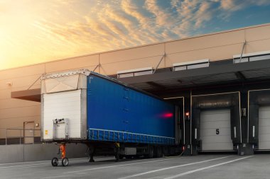 Innovative modern logistics warehouse center complex building exterior bay gate semi-trailer unloading goods distribuition warm blue sunset sky background. Cargo storage facility industry building.
