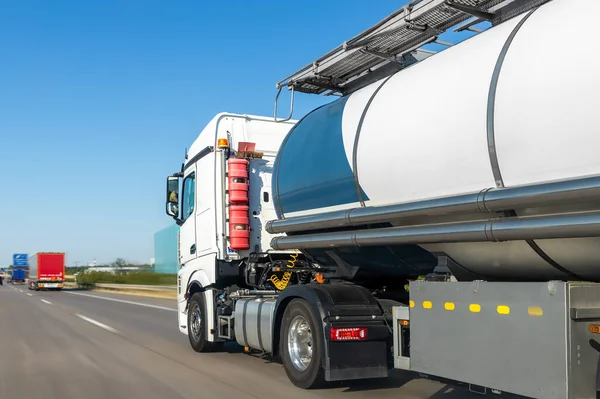 White big modern tanker shipment cargo commercial semi trailer truck moving fast on motorway road city urban suburb. Business distribution logistics service. Lorry driving highway sunny day.