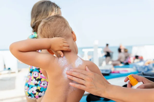 Mother applying sunscreen protection creme on cute little baby boy kid back. Mum using sunblocking lotion to protect baby from sun during summer sea vacation. Child healthcare travel vacation time.
