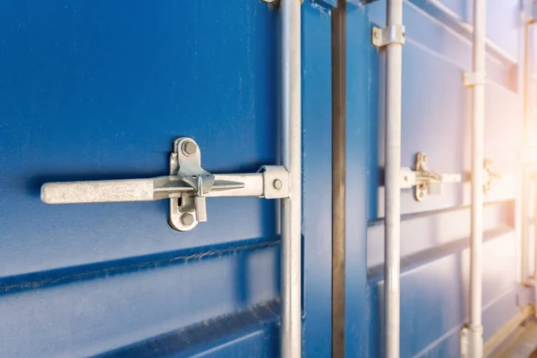 Close-up detail view of big blue metal freight cargo container door handle closed with padlock lock. Storage warehouse safety. Commercial shipping port. Export and import goods customs clearance.