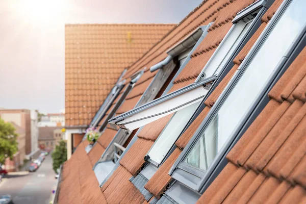 Open ventilation waterproof rooftop window exterior against sunny sky light. Velux style roof with red brick tiles. European city street attic mansard modern roofwindow service, install maintenance.