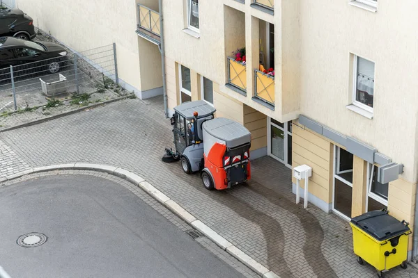 Top above view of small sweeping vacuum cleaner machine equipment removing dust rubbish city street sidewalk paved road near apartment condo building. Special municipal sweeper vehicle cleaning town.