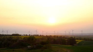 Panoramic landscape view of many modern wind turbine farm power generation station against warm sunset haze mist sky. Clean sustainable zero emission alternative electricity windfarm industry.