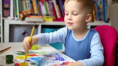 Portrait of cute little blond kid boy enjoy have fun painting with watercolor and brush bright abstract inage on paper at home or kindergarten class. Imagination development children play activity.