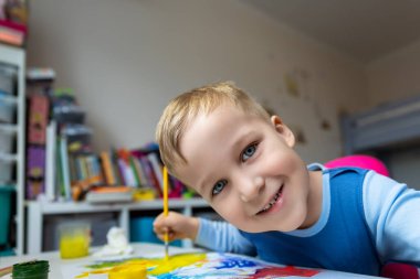 Portrait of cute little blond kid boy enjoy have fun painting with watercolor and brush bright abstract inage on paper at home or kindergarten class. Imagination development children play activity.